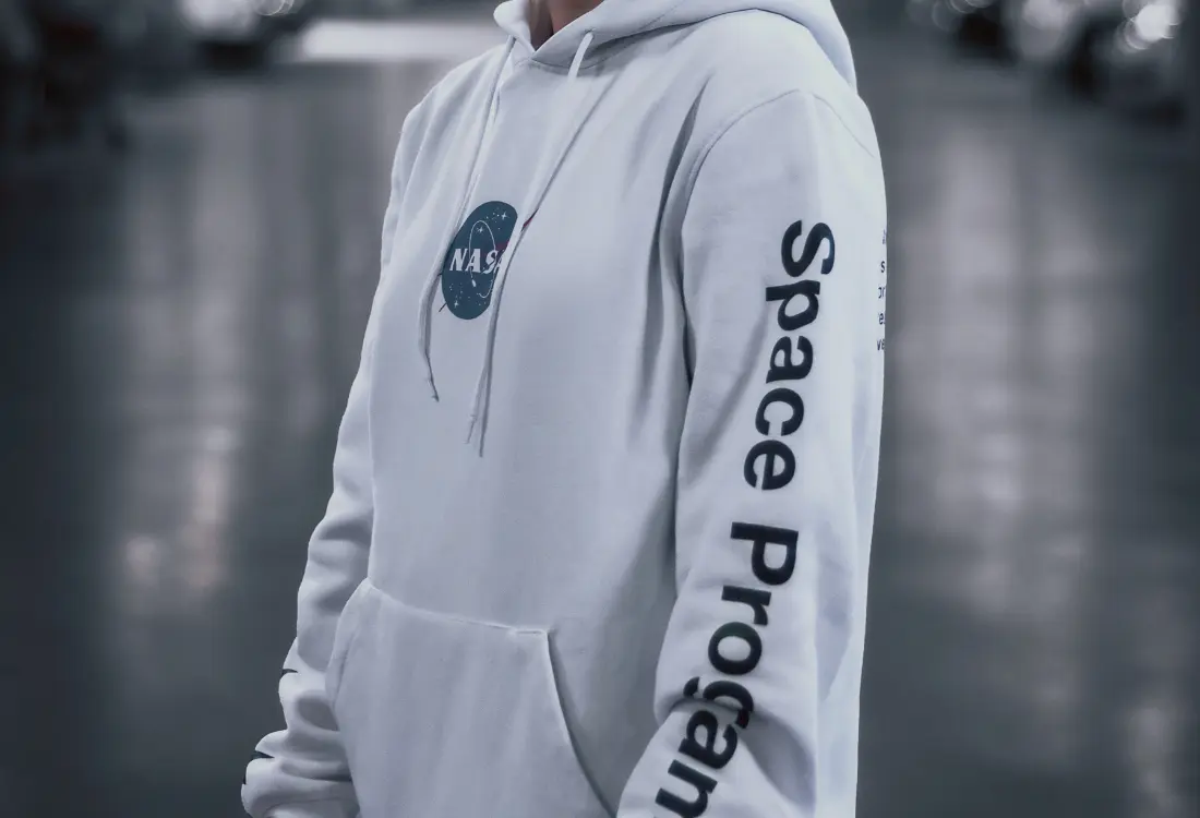 White NASA branded hoodie with logo print and sleeve design inspired by the company's mission. This is a timeless yet stylish design that highlights the brand in a sleek way.